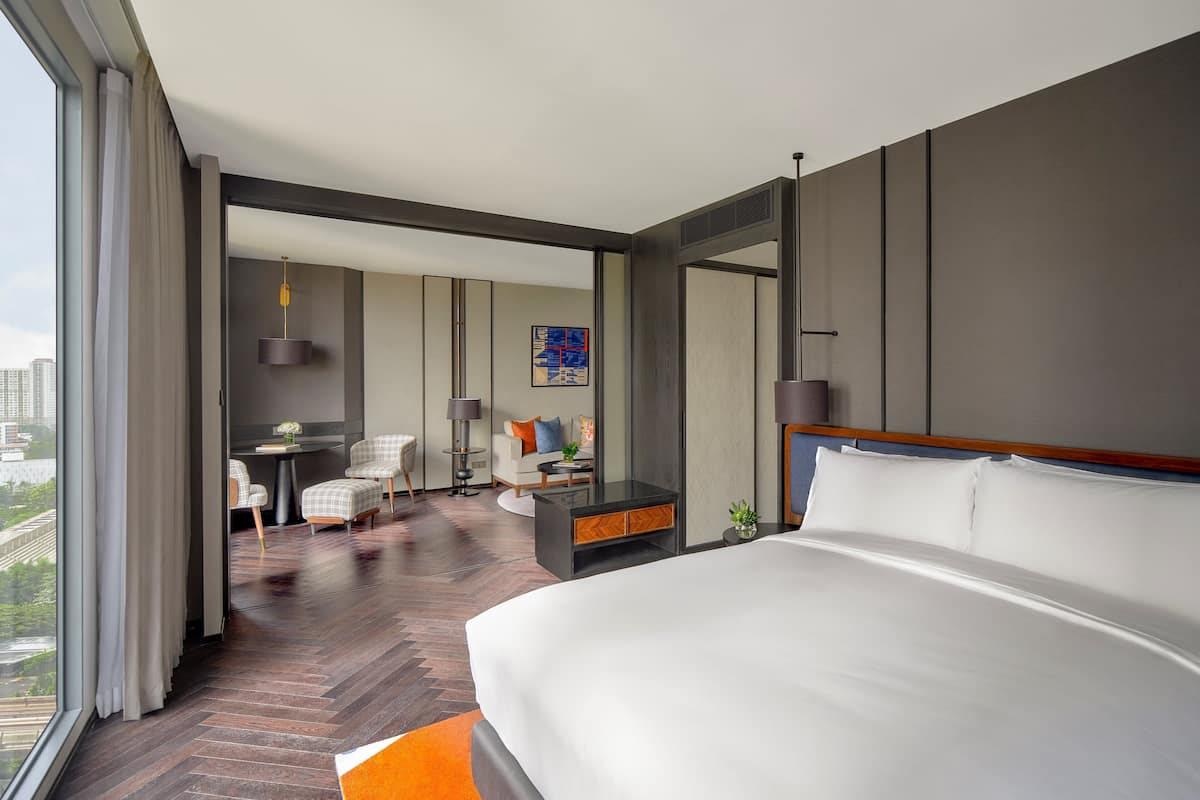A modern hotel room with a large bed, a desk, and a seating area with chairs and a table.