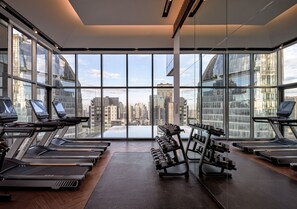 A modern gym with treadmills and dumbbells, large windows with a city view.