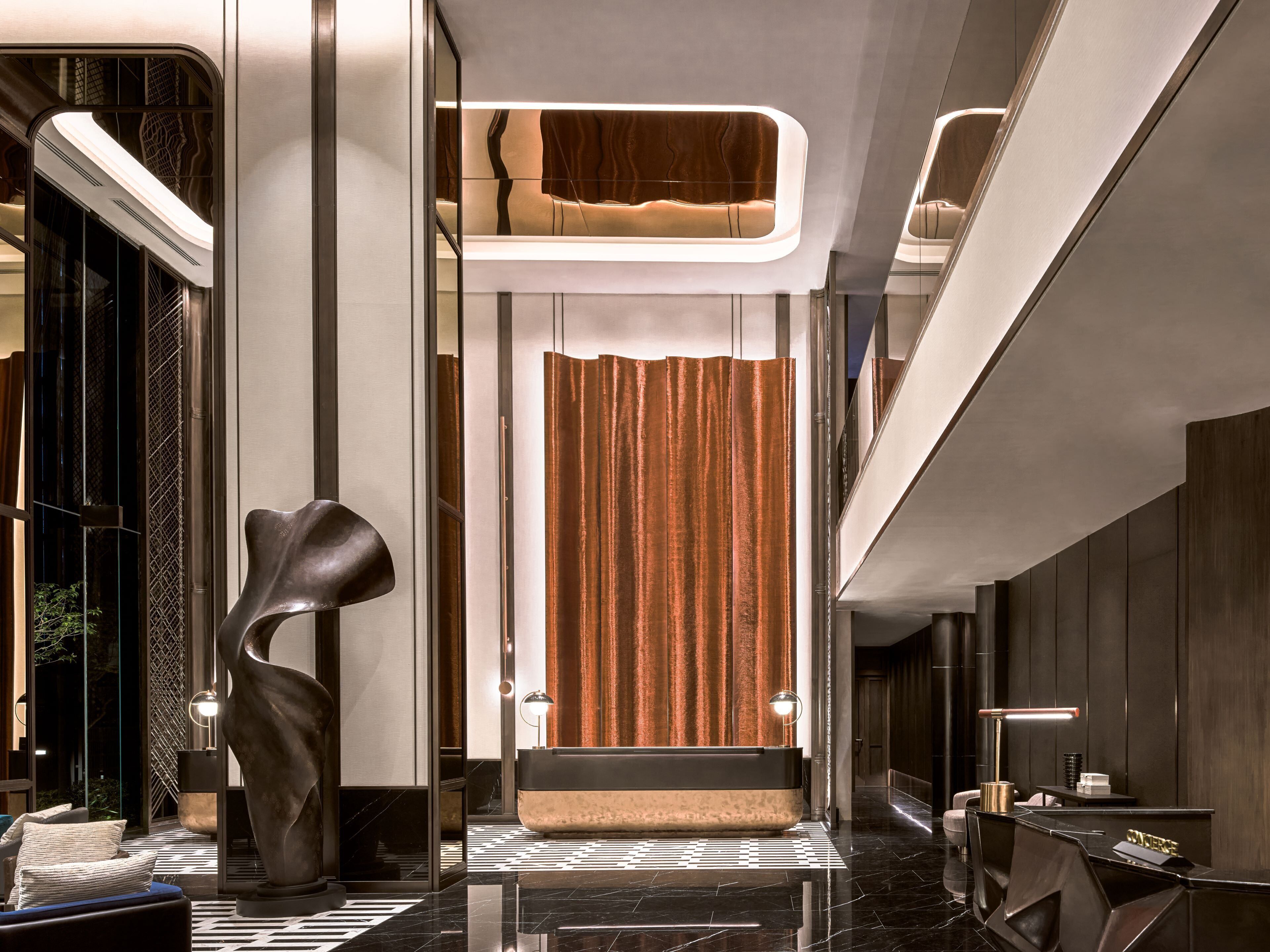 A modern lobby with a reception desk, a sculptural installation, and a patterned floor.