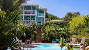 A two-story building with a pool, surrounded by lush tropical vegetation.