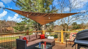 Une terrasse avec un canapé, une table basse en verre et un barbecue.