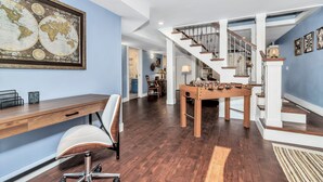 Une pièce spacieuse avec un bureau en bois, un fauteuil confortable, une table de baby-foot et un escalier menant à un autre niveau.