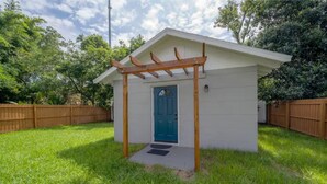 A small, single-story building with a blue door and a wooden pergola entrance.
