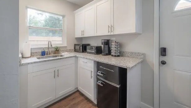 A compact kitchen with white cabinets, a stainless steel refrigerator, a microwave, a toaster, and a coffee maker.