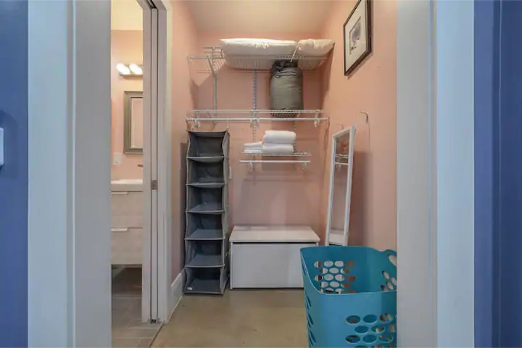 A narrow hallway with a closet containing shelves, a hanging rack, and a storage bin.
