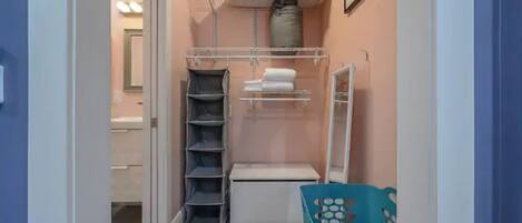 A narrow hallway with a closet containing shelves, a hanging rack, and a storage bin.