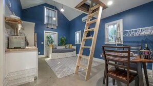 Una habitación con pared azul, una escalera de madera, una mesa de comedor con sillas y una zona de cocina con refrigerador y lavaplatos.