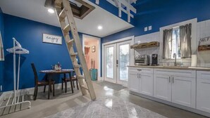 Una cocina con armarios blancos, una mesa de comedor con sillas, una escalera y un letrero que dice 'enjoy'.