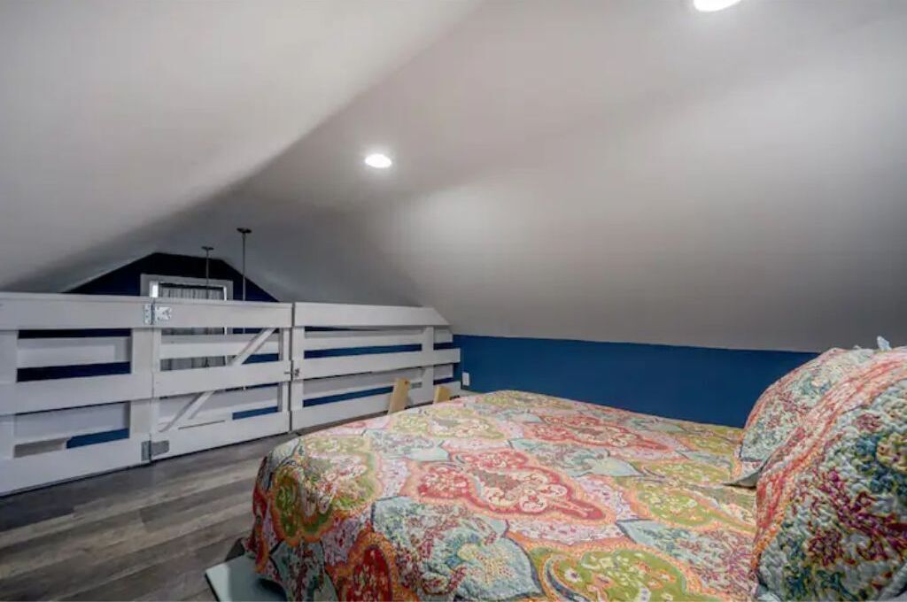 Une chambre avec un plafond en pente, un lit recouvert d’une courtepointe aux motifs colorés et un banc blanc intégré le long du mur.