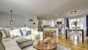 A modern living room with a sofa, coffee table, and a kitchen in the background. - NEW! Updated Mystic Home w/ Sauna, Hot Tub & Deck (Groton)