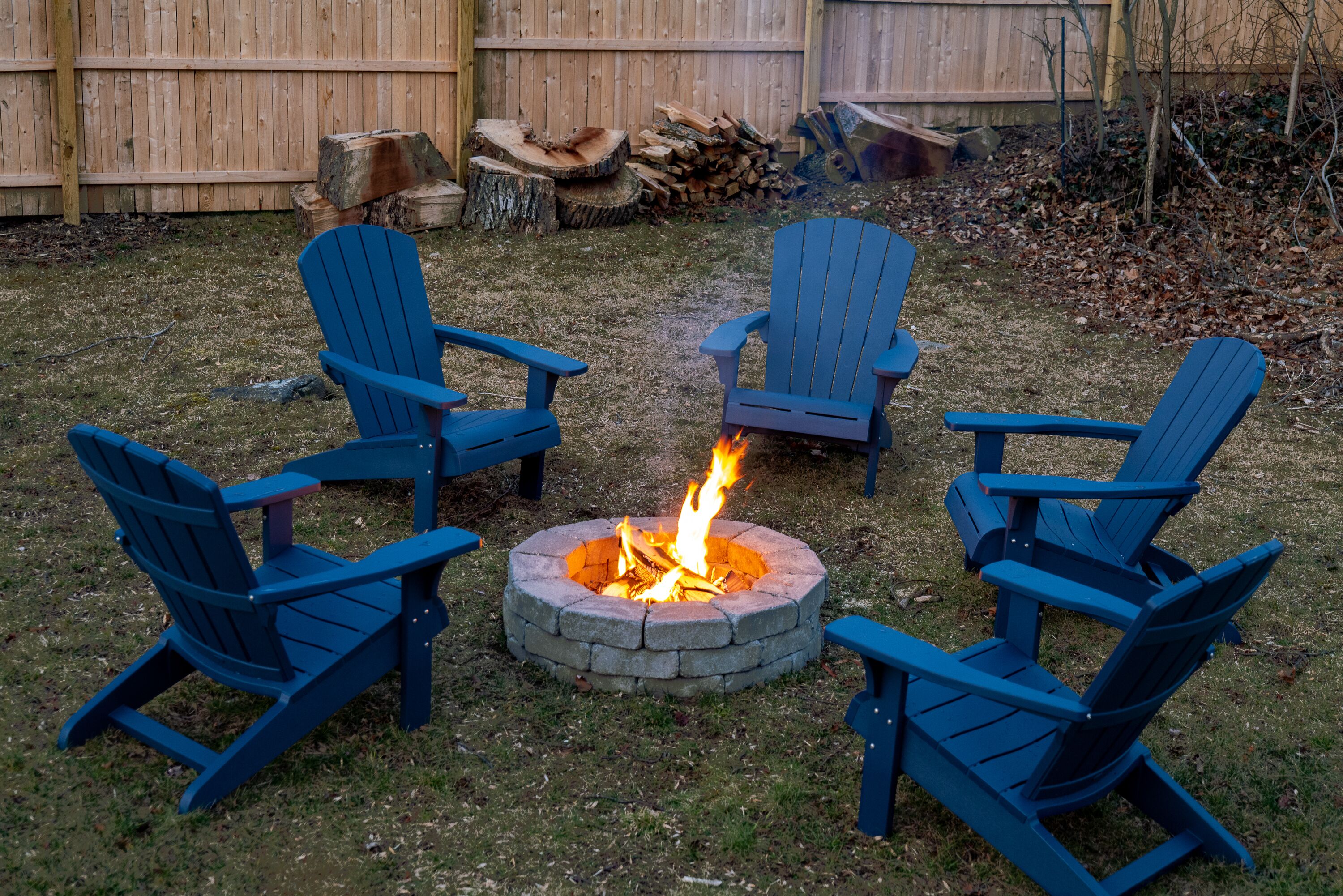 Un foyer extérieur entouré de quatre chaises Adirondack bleues, disposées autour, dans un jardin.