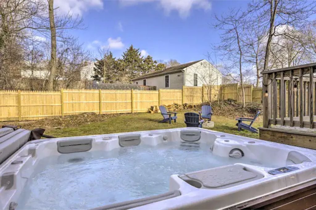 Un bain à remous dans un jardin, avec une terrasse en bois, une clôture en bois et une maison en arrière-plan.