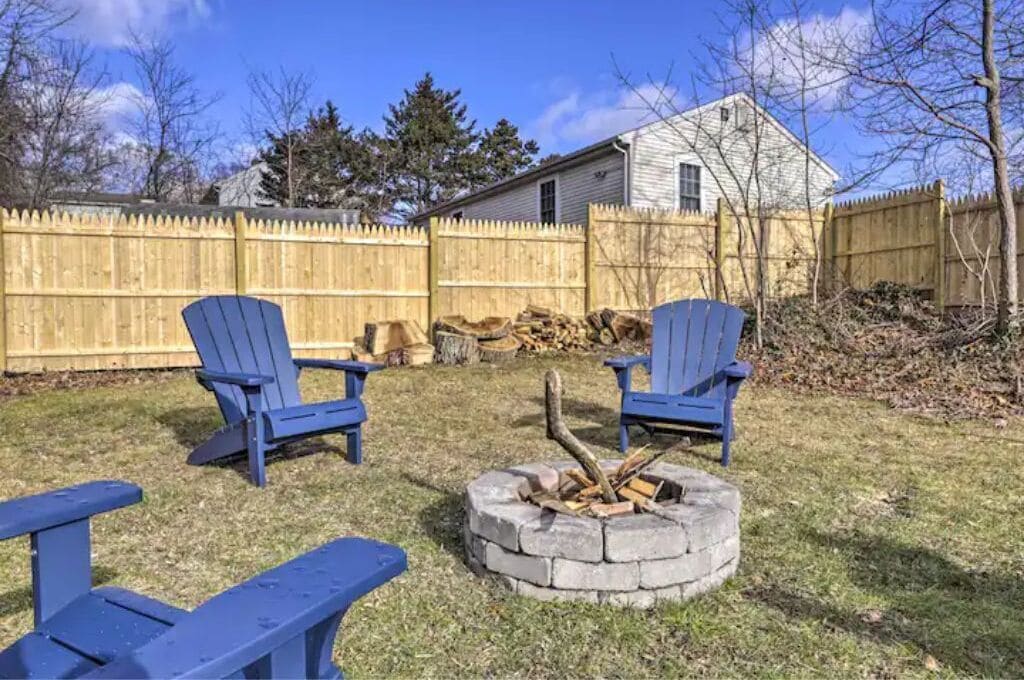 A backyard with two blue Adirondack chairs, a fire pit, and a wooden fence.