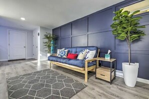 Uma sala de estar moderna com um sofá azul, um tapete geométrico e uma planta grande em vaso.