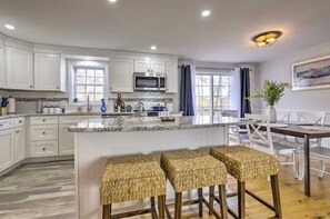 Cozinha moderna com armários brancos, uma ilha central com banquetas e uma área de jantar com mesa e cadeiras.
