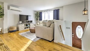 A modern living room with a sofa, TV, and a dining area with a table and chairs. - NEW! Updated Mystic Home w/ Sauna, Hot Tub & Deck (Groton)