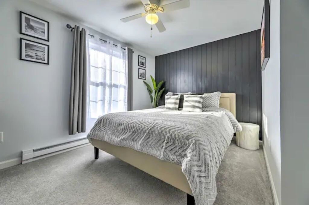 Ein Schlafzimmer mit einem Bett, einem Deckenventilator, einem Fenster mit Vorhängen und einer Pflanze.