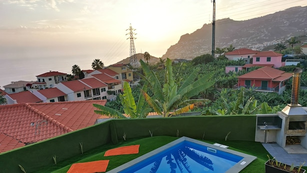 En swimmingpool med konstgräs och gula solstolar, omgiven av grönska och bostadshus i bakgrunden.