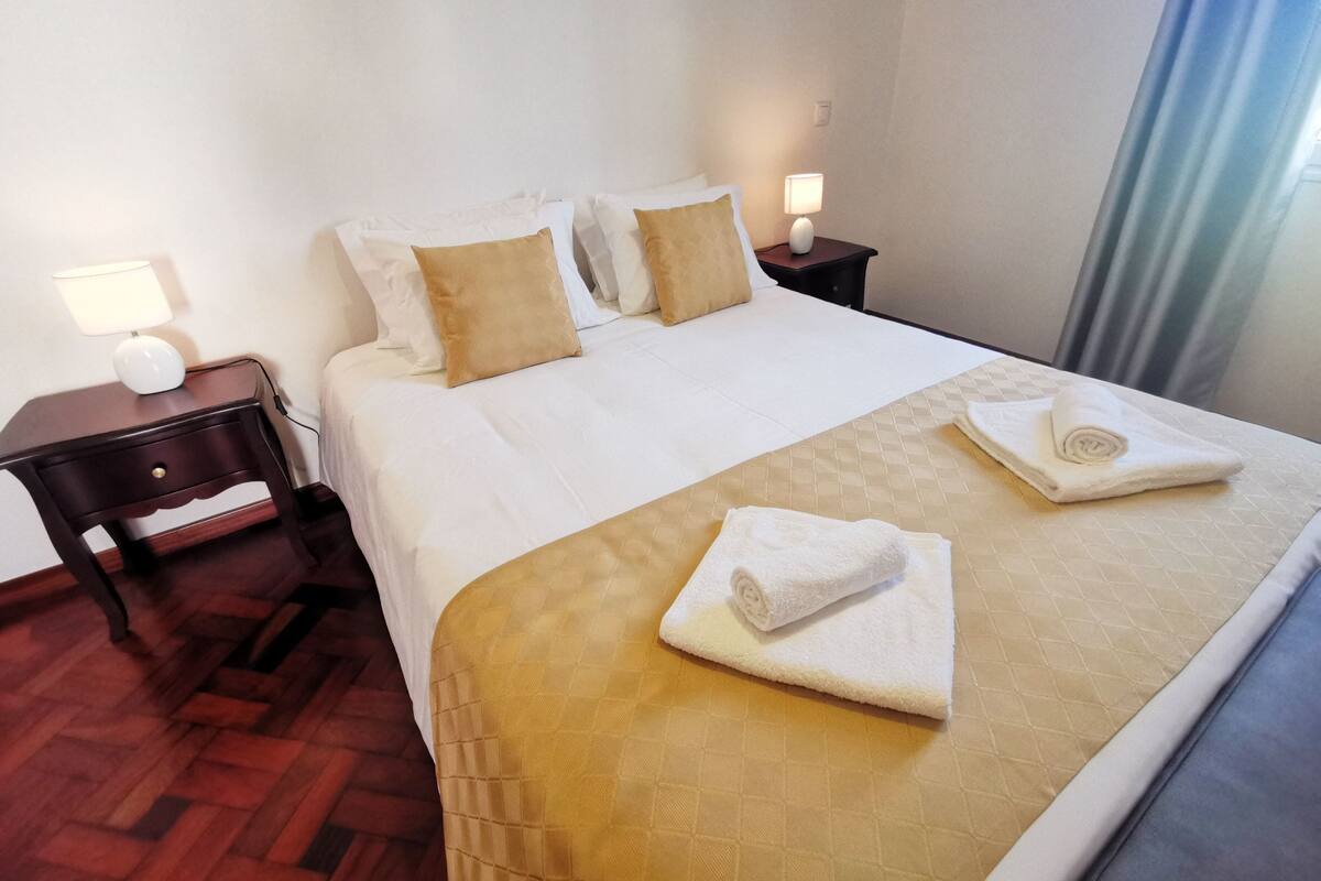 A hotel room with a bed, two bedside tables, a lamp, and a window with curtains.
