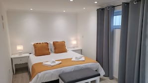 Ett modernt hotellrum med en väl bäddad säng, två sängbord med lampor, en bänk och grå gardiner.