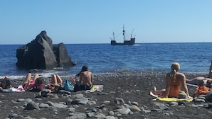 En strand med folk som solar och en stor klippformation.