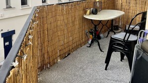Un balcón con mesa y sillas, una valla de bambú y vistas de edificios circundantes.