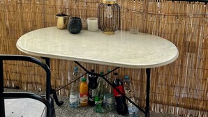Una mesa redonda con superficie blanca, rodeada por una valla de bambú, con botellas y una pequeña planta en maceta sobre el suelo.
