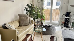 Una sala de estar moderna con un sofá color beige, una mesa de centro de vidrio, un sillón de cuero rojo y diversas plantas.