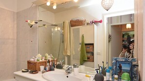 Un baño con un espejo grande, un lavamanos y diversos artículos de aseo.