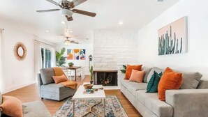 A modern living room with a fireplace, grey sofas, and a ceiling fan. - Luxury Tropical Modern Pool Estate/NO PARTIES (San Bernardino)