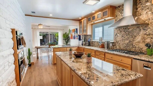 A modern kitchen with granite countertops, wooden cabinets, and stainless steel appliances. - Luxury Tropical Modern Pool Estate/NO PARTIES (San Bernardino)