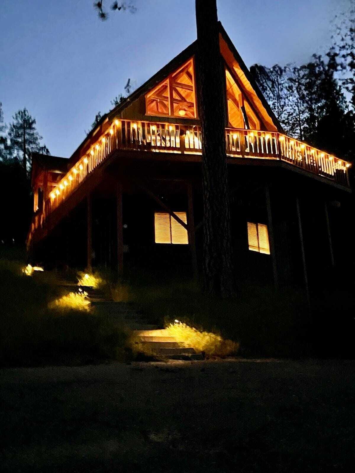 Une cabane en bois dotée d’un balcon, illuminée par des guirlandes lumineuses.