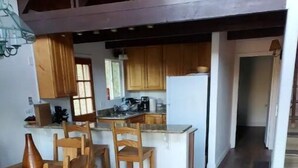 A modern kitchen with wooden cabinets, a central island, and a dining area with wooden chairs. - Serenity View, Peaceful & Cheerful 3BD Cabin. (Groveland)