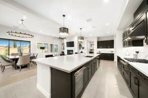 A modern kitchen with a large island, dark cabinetry, and pendant lighting. - New Luxury La Quinta Resort Home (La Quinta)