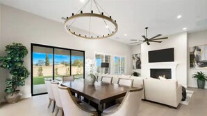 Una sala de estar moderna con comedor, ventanas amplias, chimenea y ventilador de techo.