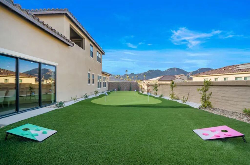 Un giardino curato con erba sintetica, un putting green e due tavolini.