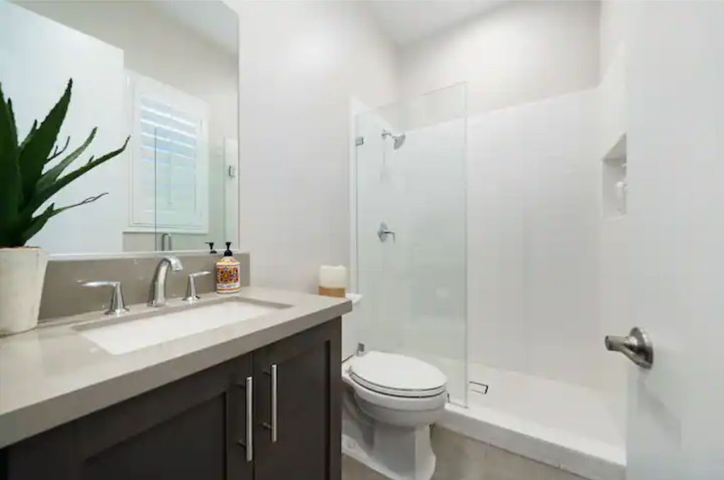 Een moderne badkamer met een douchecabine van glas, een wit toilet en een wastafel met een spiegel en twee wasbakken.