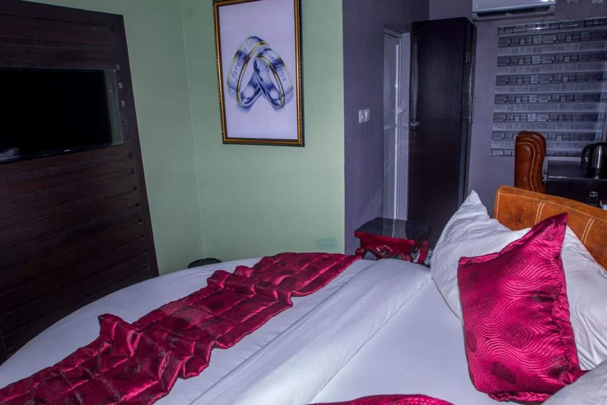 Hotellihuone, jossa on sänky, seinällä kehystetty taulu, ilmastointilaite ja puinen pääty.