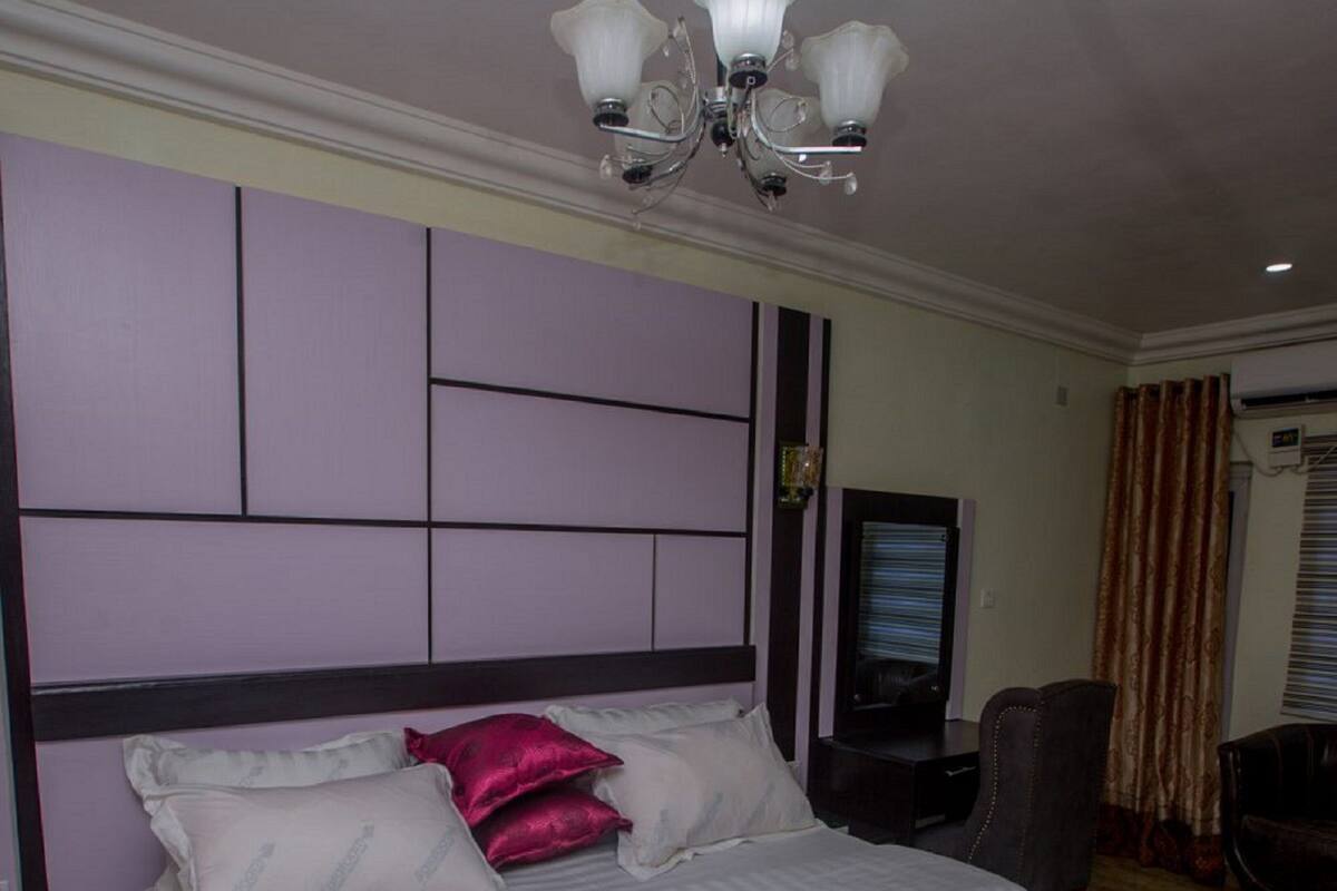 Hotellihuone, jossa on suuri sänky, televisio, tuoli ja kattokruunu.