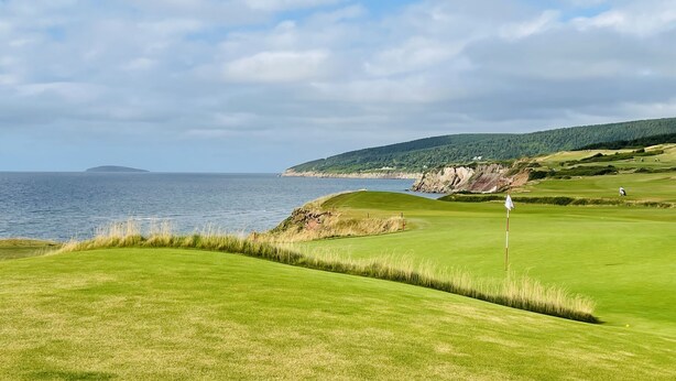 A golf course with a water body and hills in the background.