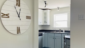 A kitchen with light blue cabinets, a large wall clock, and a window providing natural light.