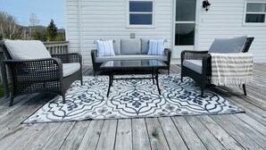 A deck with a sofa and two chairs, a glass table, and a patterned rug.