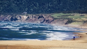 A beach with waves, a person standing, and a house in the background.