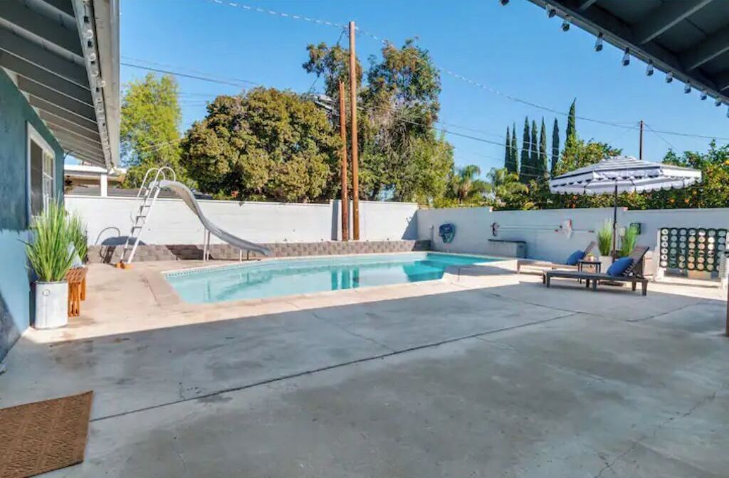A backyard with a swimming pool, a slide, and lounge chairs.