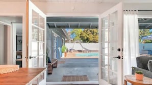 Eine offene Tür, die in einen Garten mit Pool, Rutsche und einer Holzterrasse führt.