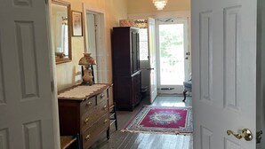 A hallway with a wooden floor, a red and blue patterned rug, a chandelier, and a large mirror on the left wall. - The Sautee Inn Bed & Breakfast (Sautee Nacoochee)