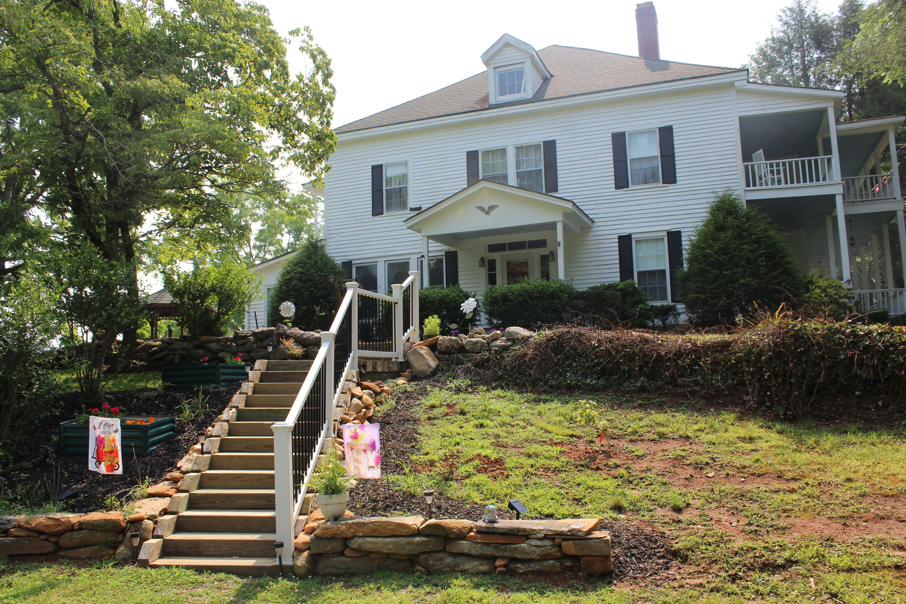 A two-story house with a front porch, stone steps, and a small garden area.
