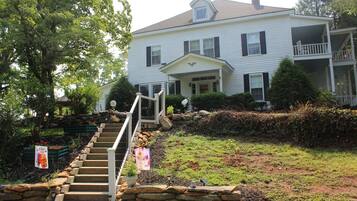 A two-story house with a front porch, stone steps, and a small garden area.