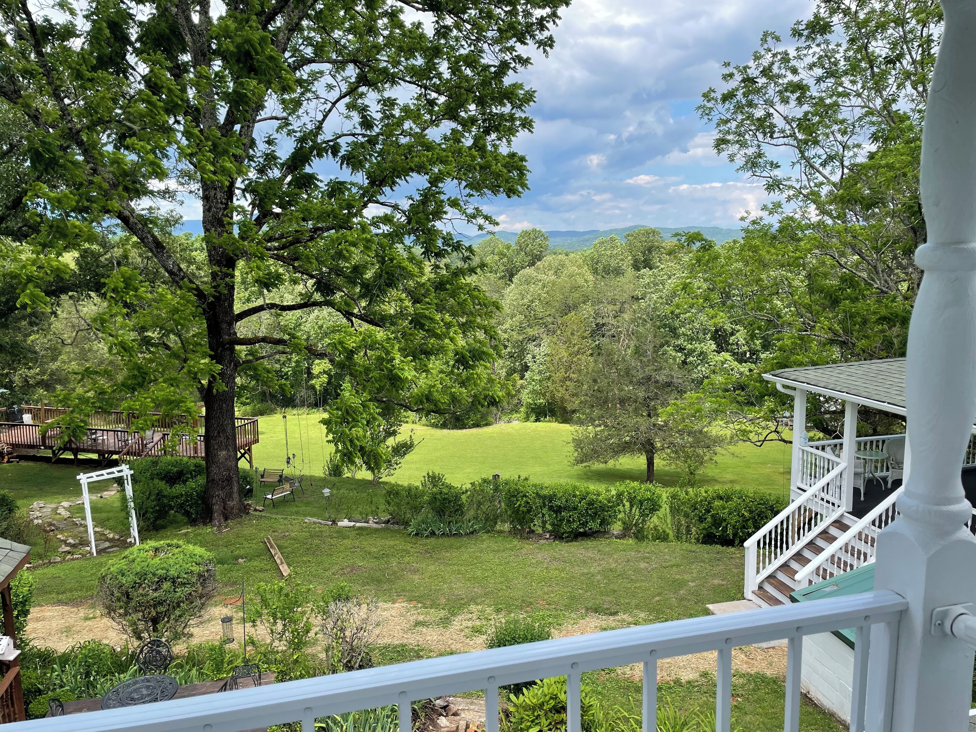A view from a porch overlooking a well-maintained lawn with a swing set, a wooden deck, and a white railing.