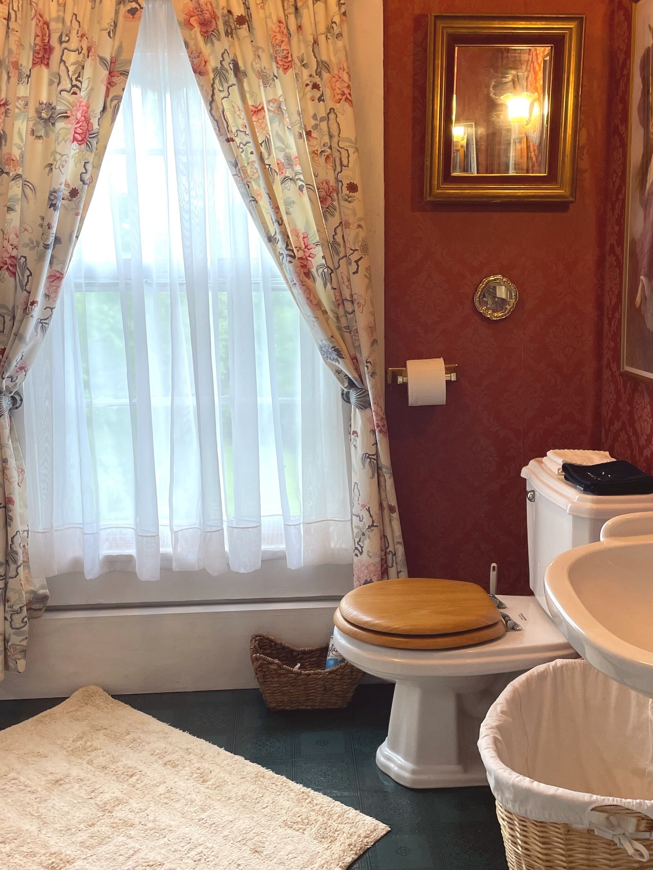 Un baño con inodoro, bidé y ventana con cortinas florales.